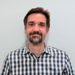 Man with a beard smiling, wearing a blue and white checkered shirt.