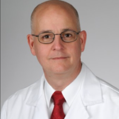 Bald man in white lab coat and red tie.