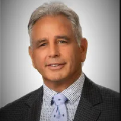 Portrait of a man in a gray suit and blue tie smiling.