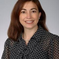Portrait of a woman with brown hair wearing a black patterned shirt.