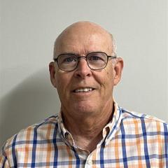 Portrait of a smiling older man in an orange and blue plaid shirt.