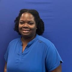 Woman smiling in front of blue backdrop, wearing blue shirt.