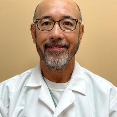 Smiling man in white coat, wearing glasses, with name tag.
