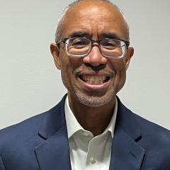 Smiling man in blue blazer over white shirt with glasses and short hair.