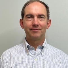 Man in a blue and white checkered shirt smiling at the camera.