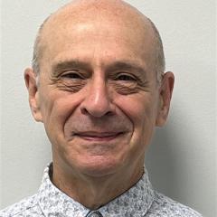 Headshot of a bald man wearing a patterned shirt, smiling at the camera.