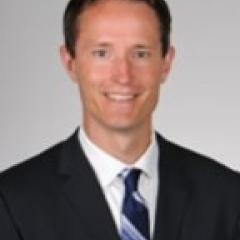 Man in black suit and blue and white striped tie smiling for the camera.