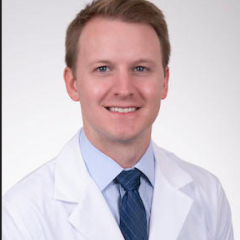 Man in white lab coat and blue tie smiling for the camera.