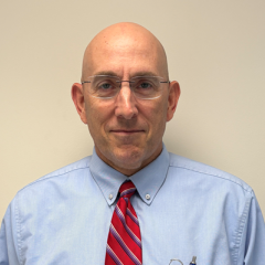 Bald man in blue shirt and red striped tie smiling.