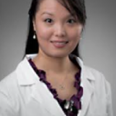 Woman in white lab coat and purple blouse smiling at the camera.