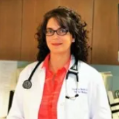 Female doctor with curly hair and glasses wearing white lab coat and stethoscope.