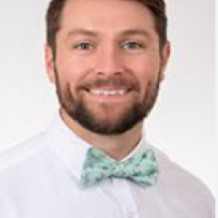 Man in white shirt with teal bowtie smiling at camera.