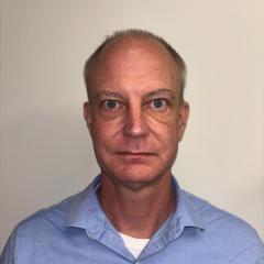 Portrait of a man with short hair wearing a blue shirt.
