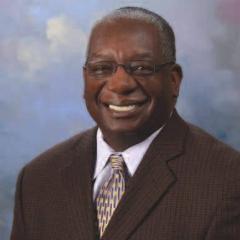 Portrait of a man in a brown suit and tie smiling.