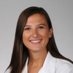 Woman with long brown hair smiling, wearing a white lab coat.