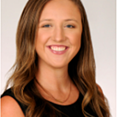 Woman with long brown hair and black top smiling for a photo.