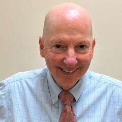 Bald man in blue shirt and red tie smiling.