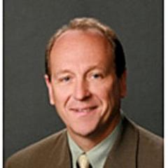 Photo of a man in a suit and green shirt smiling.
