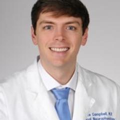 A man in a white lab coat and blue tie smiles for the camera.