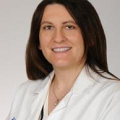 A smiling woman in a white lab coat with a blue logo.