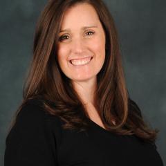 Woman with brown hair smiling at camera. Gray background.