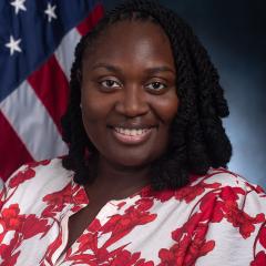 Woman with braided hair smiling in front of an American flag.