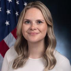 Portrait of a woman with blonde hair smiling in front of an American flag.