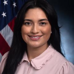 Woman with long black hair smiling in front of an American flag.