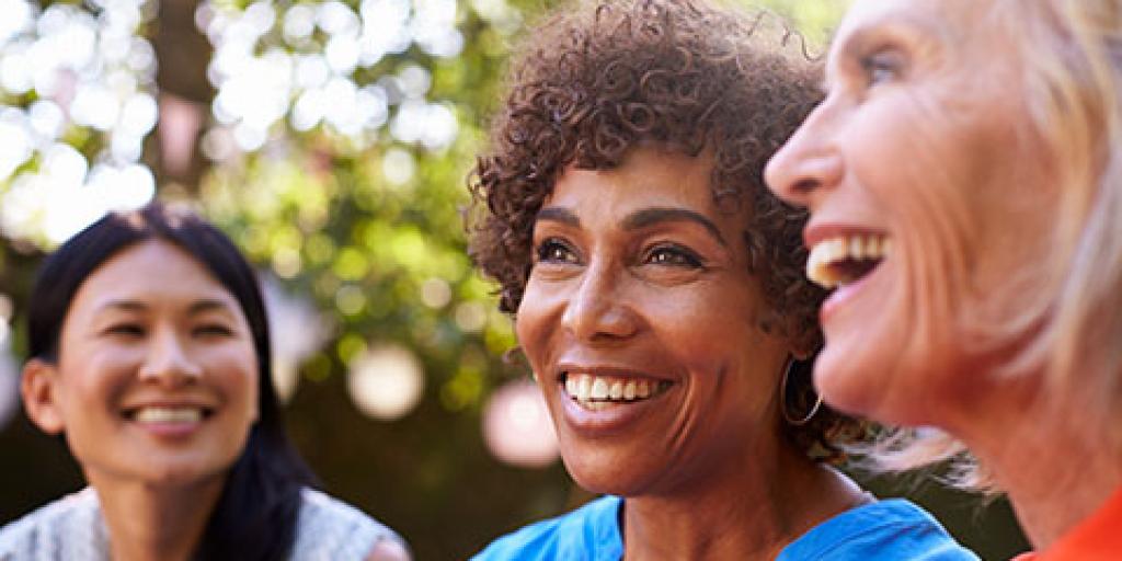 Photo of three middle aged women, multicultural, laughing together