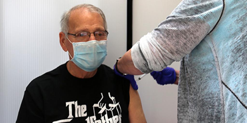 Gary Giorno, a Vietnam era Veteran in a black t-shirt and glasses looks straight ahead as he receives his second dose of the Moderna COVID-19 vaccine.