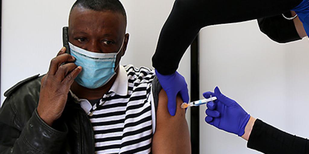 Reginald Draughn talks on the phone while the nurse delivers his first dose of the Moderna COVID-19 vaccination.
