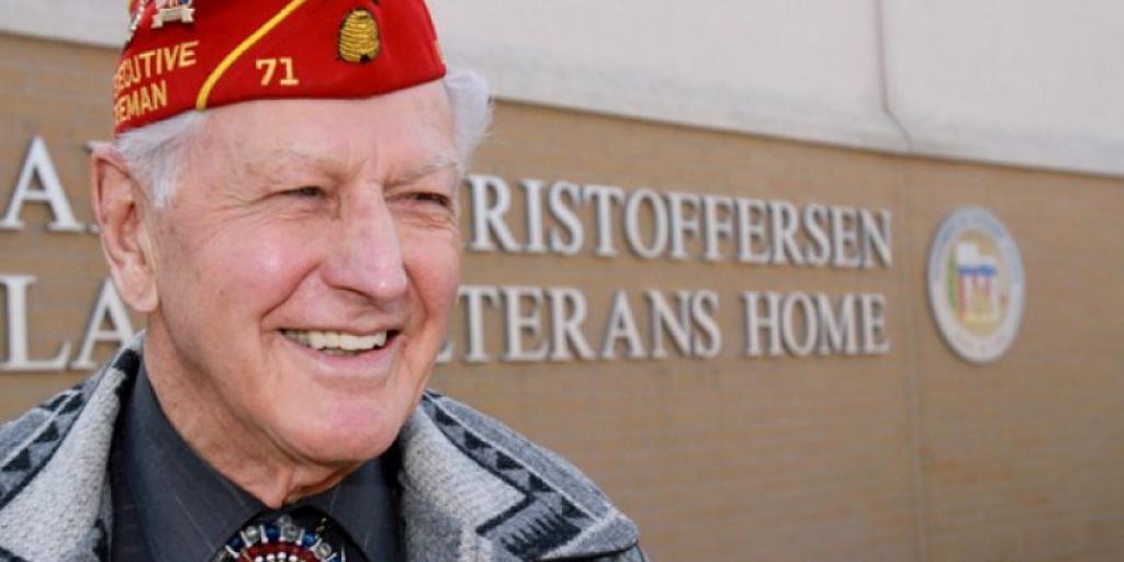 World War II Veteran and legionnaire William E. Christoffersen smiles in front of the state Veterans home that bears his name.