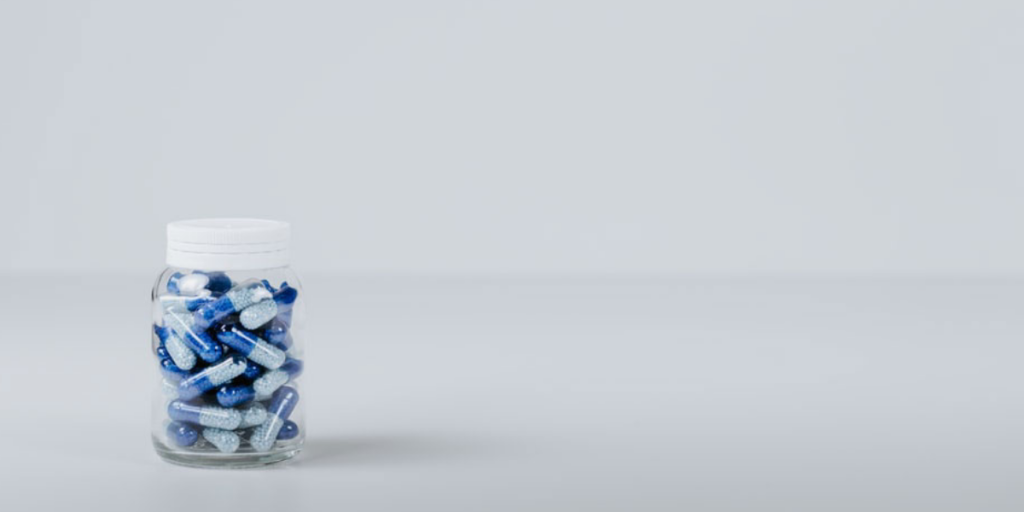 Photo of blue and white pills in a clear plastic bottle against a white-gray backdrop.