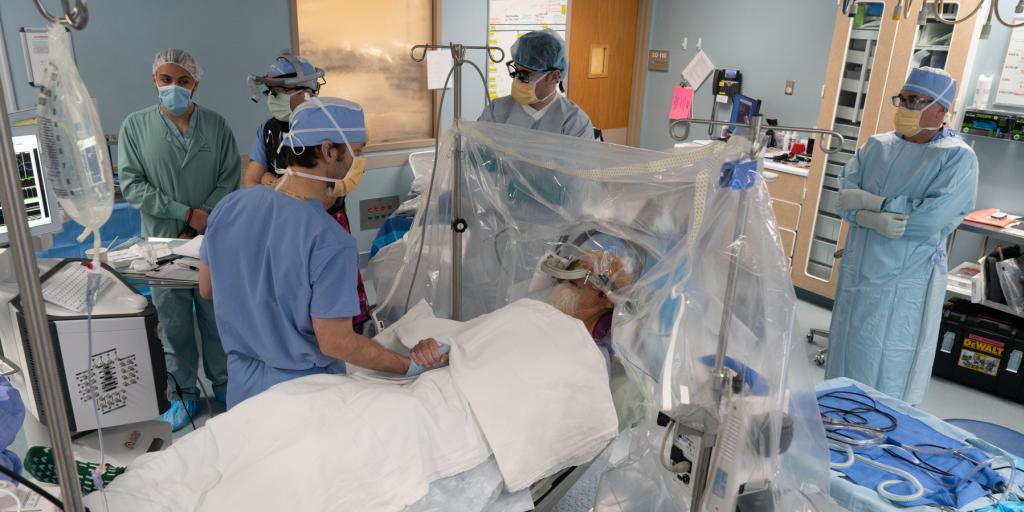 photo of surgeons wearing scrubs standing around an operating table; there is a patient on the table