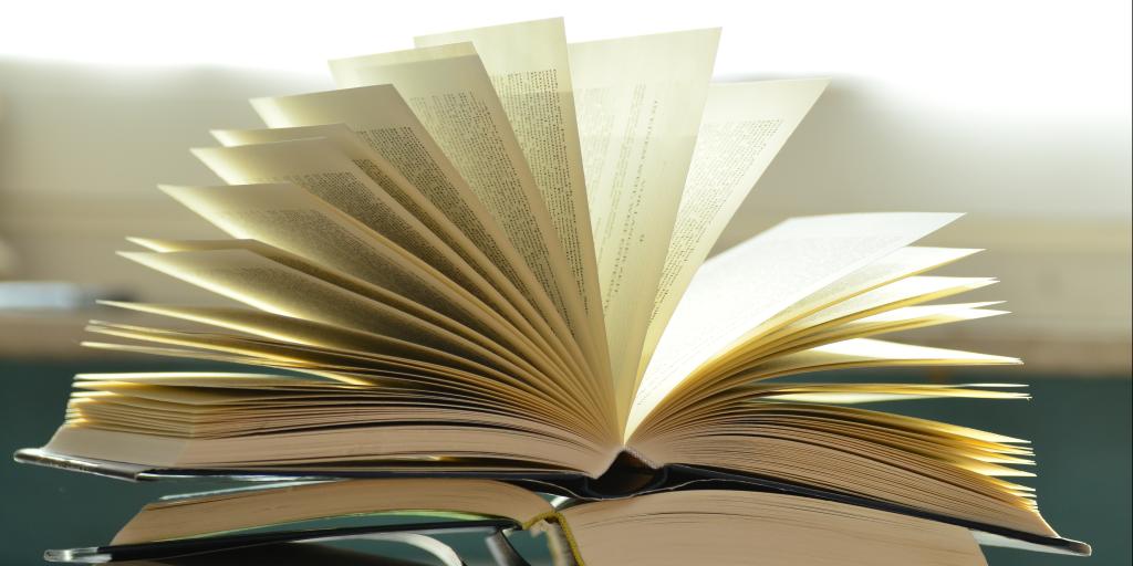 Photo depicts a pile of hardcover books with the pages open.