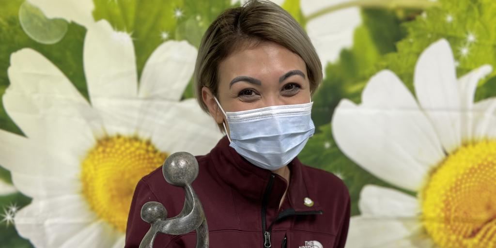 Megan holds her award in front of a yellow and green backdrop