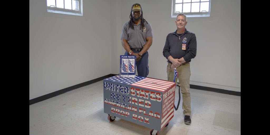 Two men standing behind a box decorated with stars and stripes in red, white, and blue