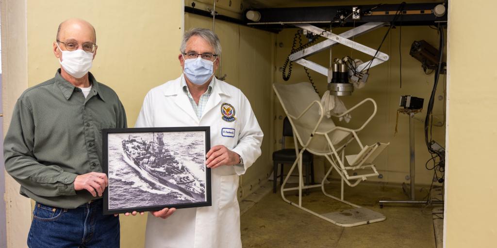 Dr. Nicholas Friedman and Paul Kanabrocki hold a picture of the USS Indiana in front of Edward Hines, Jr. VA Hospital's retired whole-body radiation counter. The device was completed in 1966 using 65 tons of the USS Indiana and was retired in 1995.