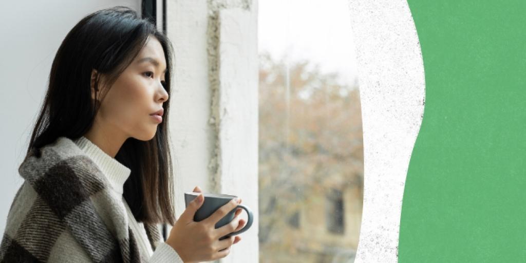 Woman holding coffee mug looking out window.