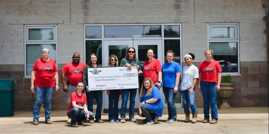 Rock Band 3 Doors Down holds $15,000 donation check with Veterans and staff members outside horse stable.