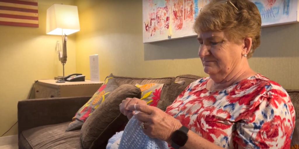 Ruby Thomas knitting while she sits in the Fisher House living room.