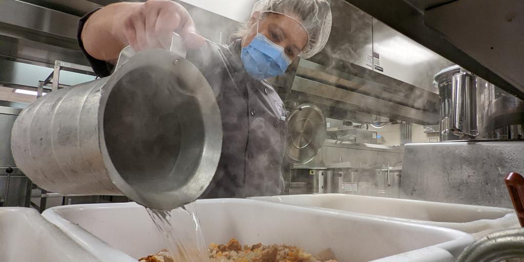 Chef adding steaming hot water to Thanksgiving meal stuffing mixture.