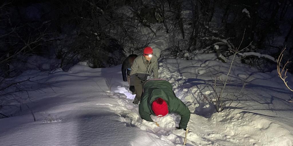 Three men climbing a hill covered with snow.