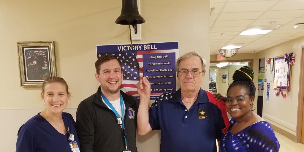 Veteran rings bell flanked by cancer care therapists