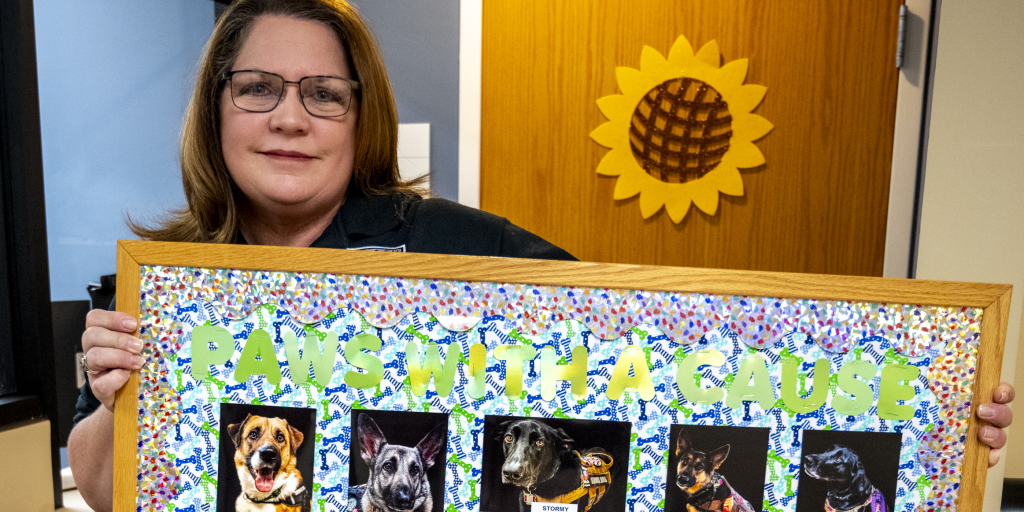Aurora CBOC security guard Kris Lohmar holds a bulletin board with her photos of service dogs.