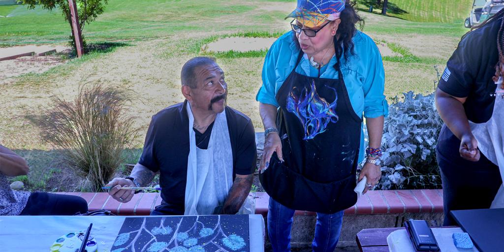 Man is instructed by a woman on painting techniques.