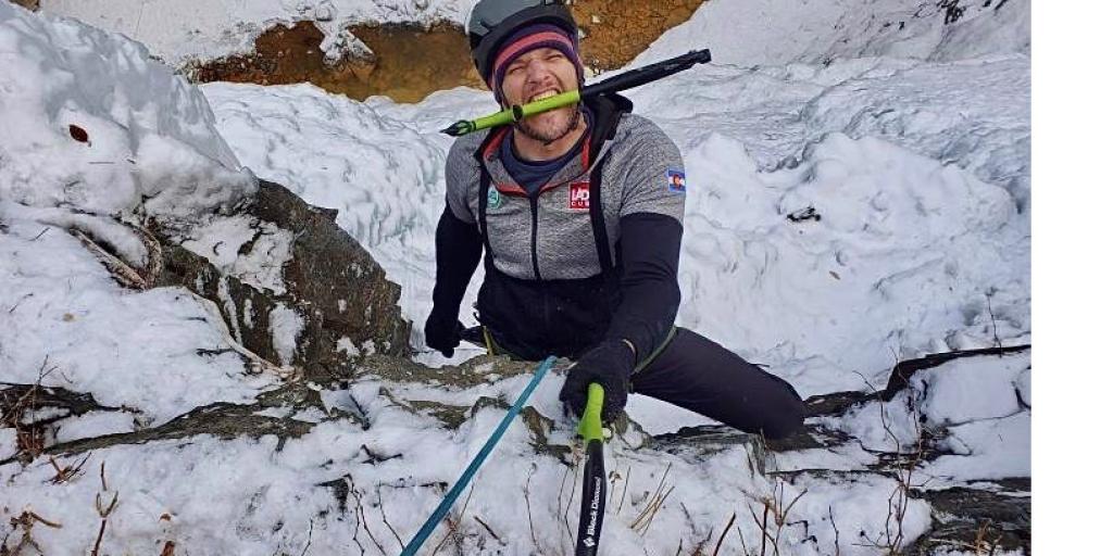 Man hanging from snowy mountain with climbing tool in mouth