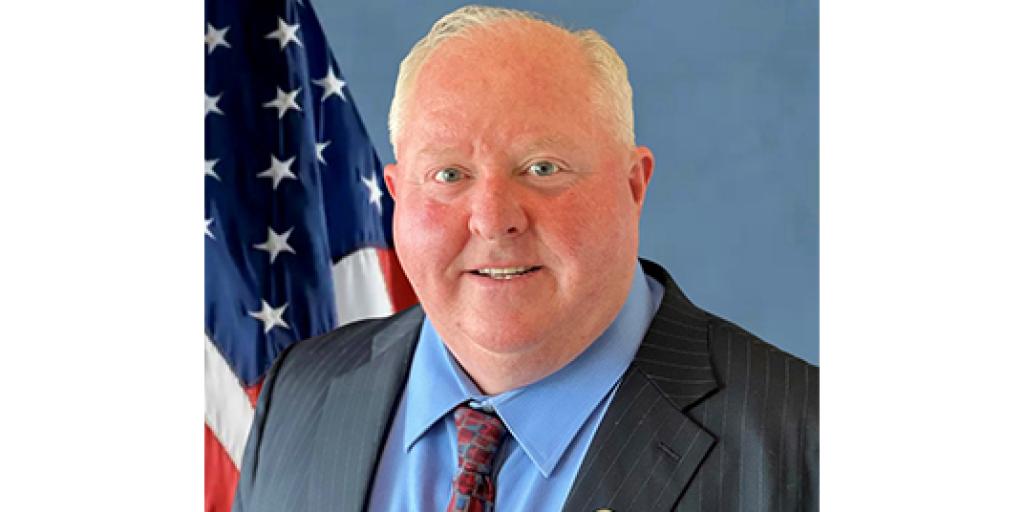 Man in suit jacket and tie in front of U.S. flag