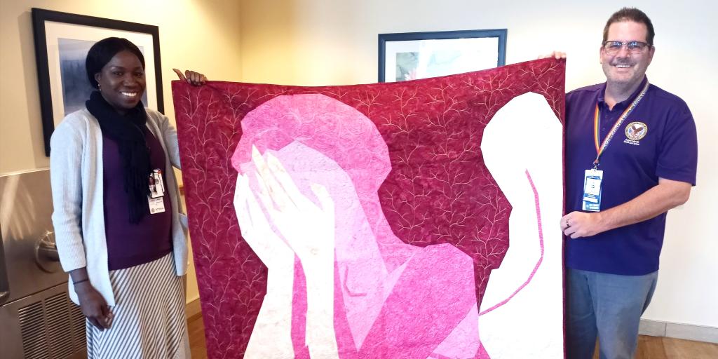 Man and woman hold large quilt with image of an angel.