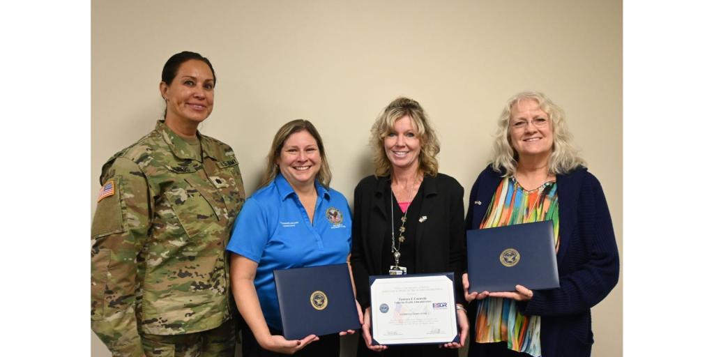 Four women, one in military uniform, stand together smiling after an award presentation.